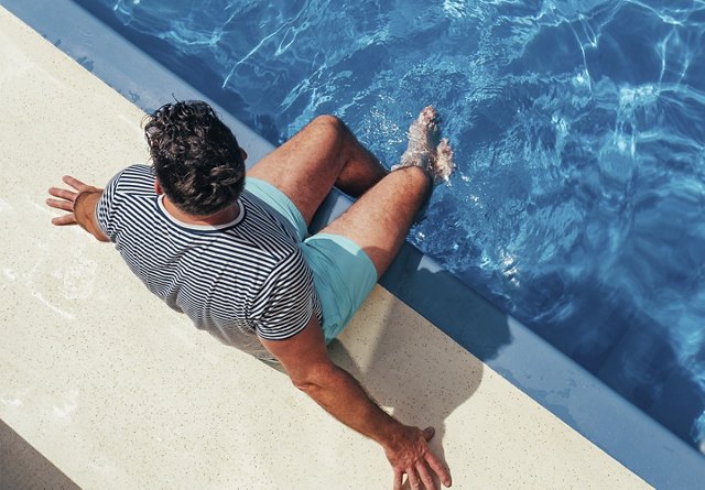 A man sitting at the edge of a pool with his feet in the water.