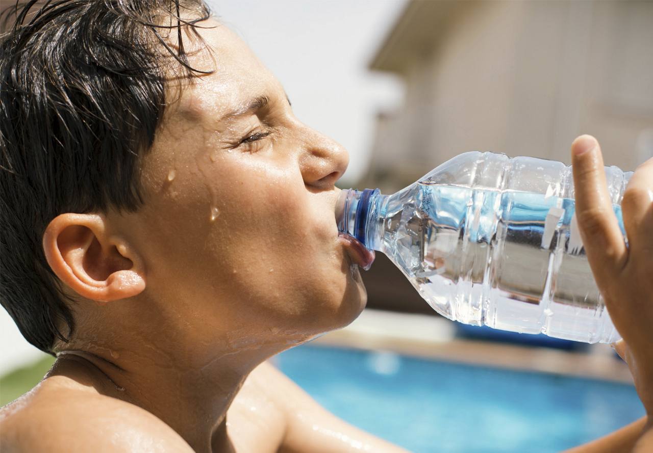 A boy drinking water by the pool.