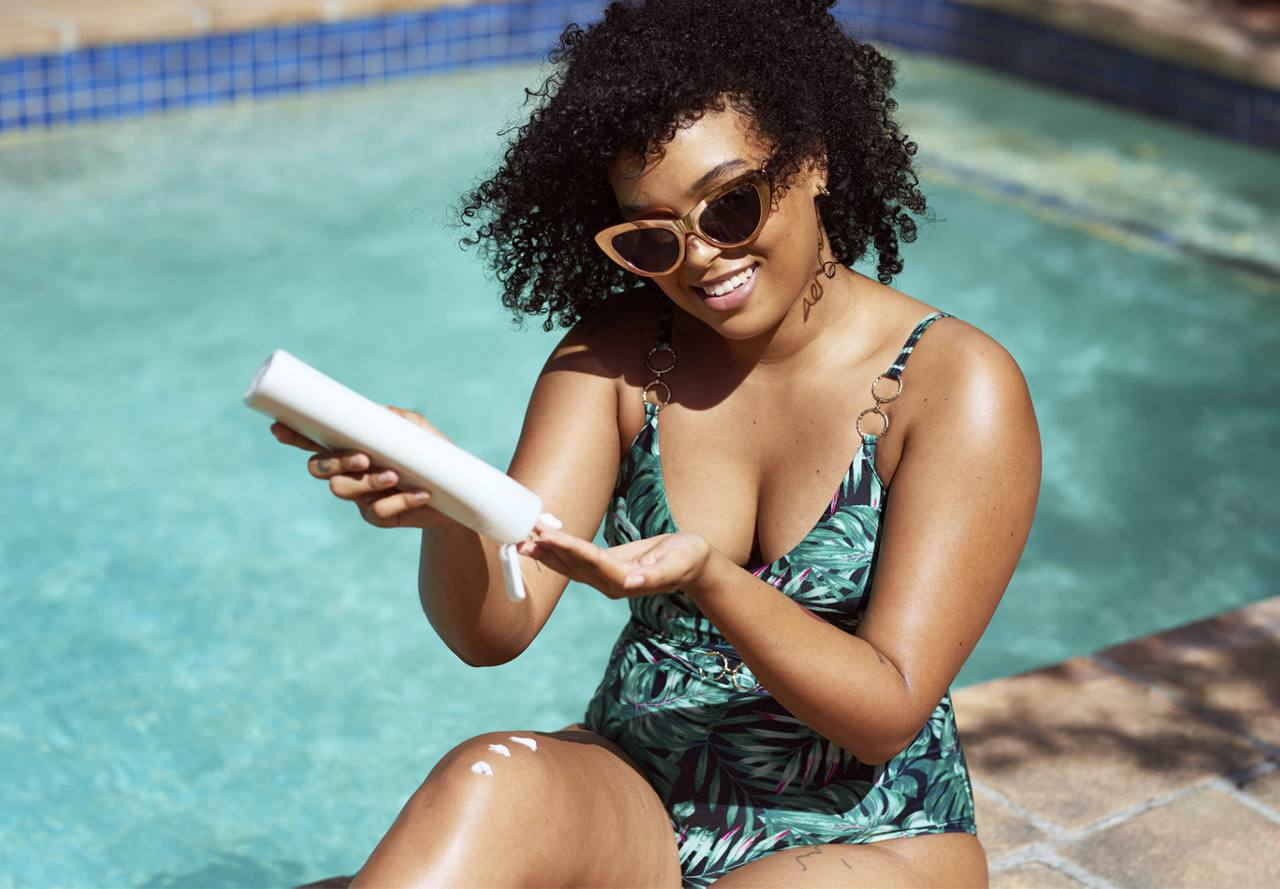 Person applying sunscreen while sitting next to a pool.