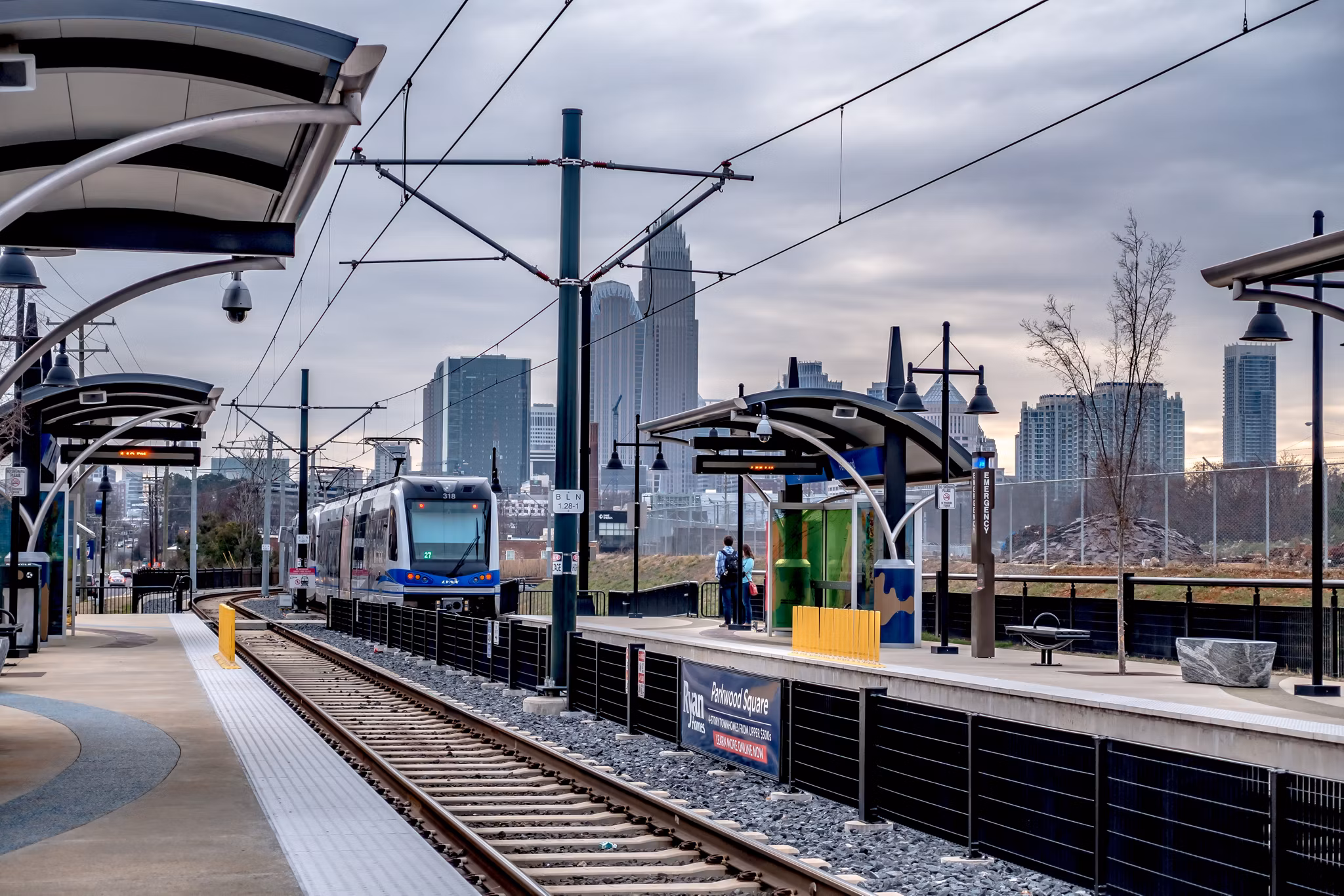 LYNX Blue Line light rail serving a station platform in Charlotte, North Carolina, with the Uptown skyline behind it — part of the CATS transit network covered in Greystar's guide to getting around Charlotte without a car.