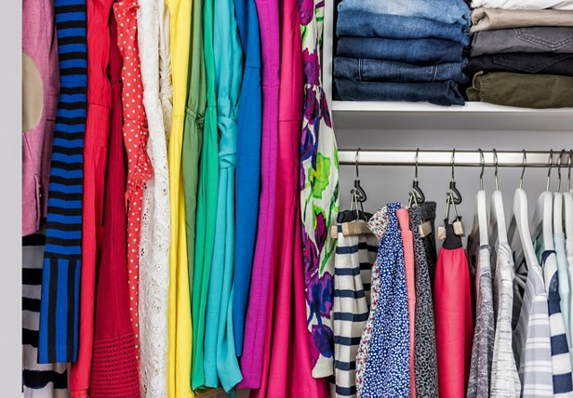 Brightly colored clothes neatly organized in a closet with folded jeans and shirts on shelves.