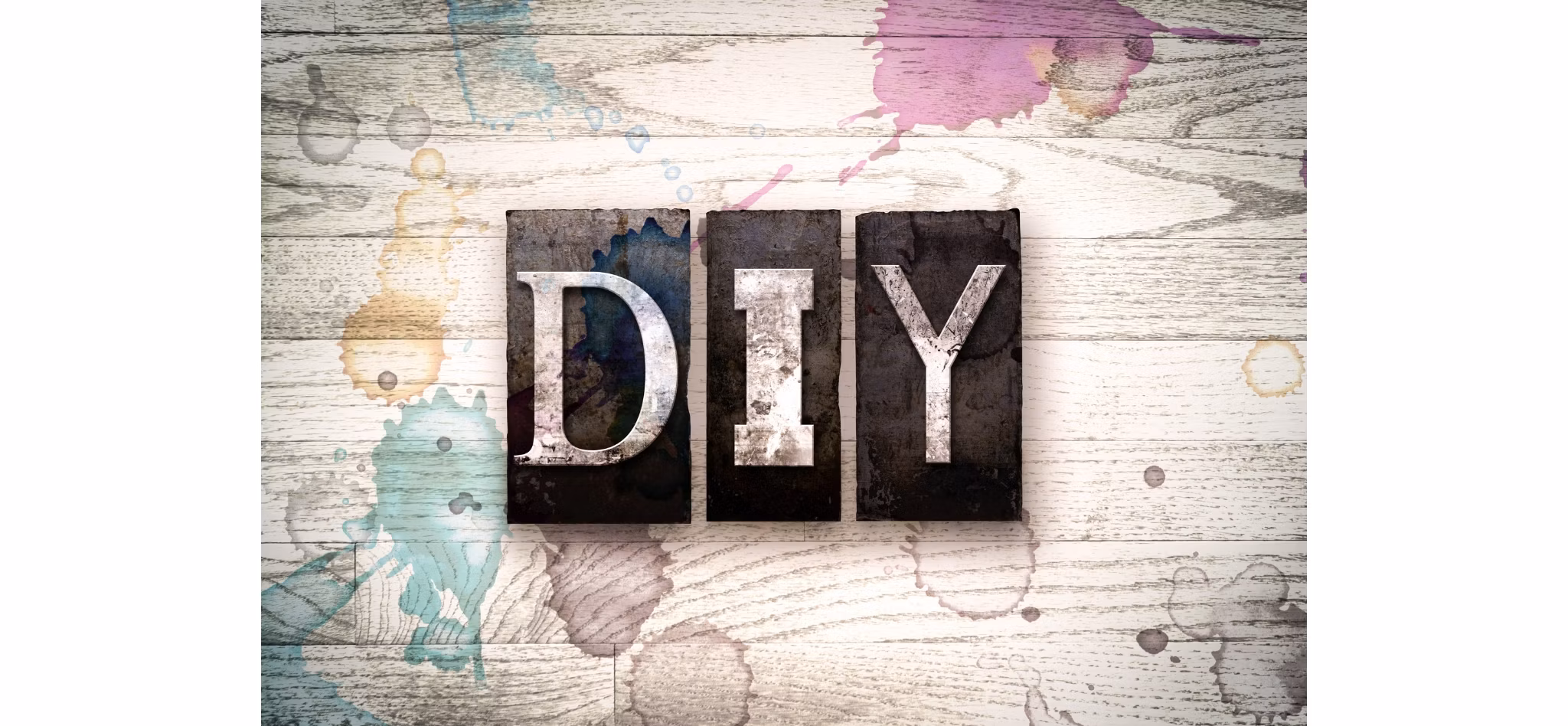 The letters 'DIY' in distressed metal typography on a wooden background with paint splatters.