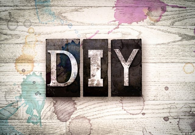 The letters &apos;DIY&apos; in distressed metal typography on a wooden background with paint splatters.