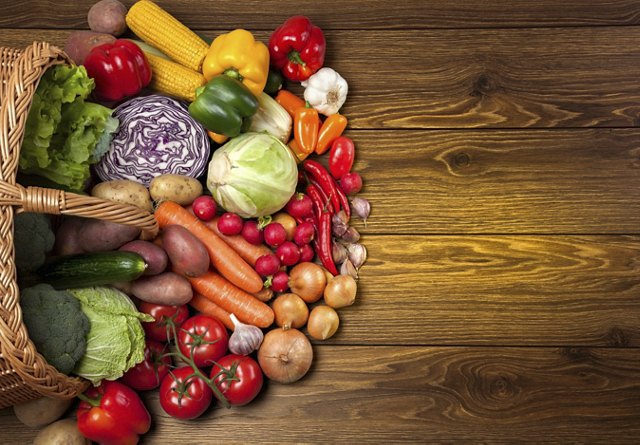 Fresh vegetables next to the overturned basket on the wooden surface.