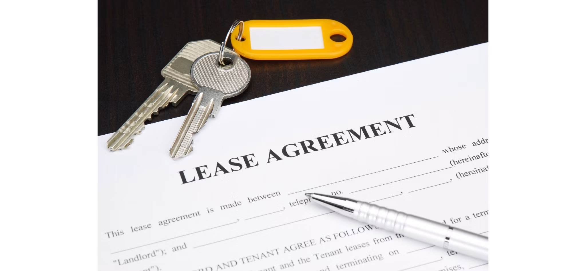 A set of keys on a lease agreement document with a pen, indicating a new rental or lease signing.