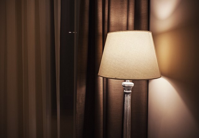 An elegant floor lamp with a beige shade casts a warm glow against a backdrop of dark curtains.