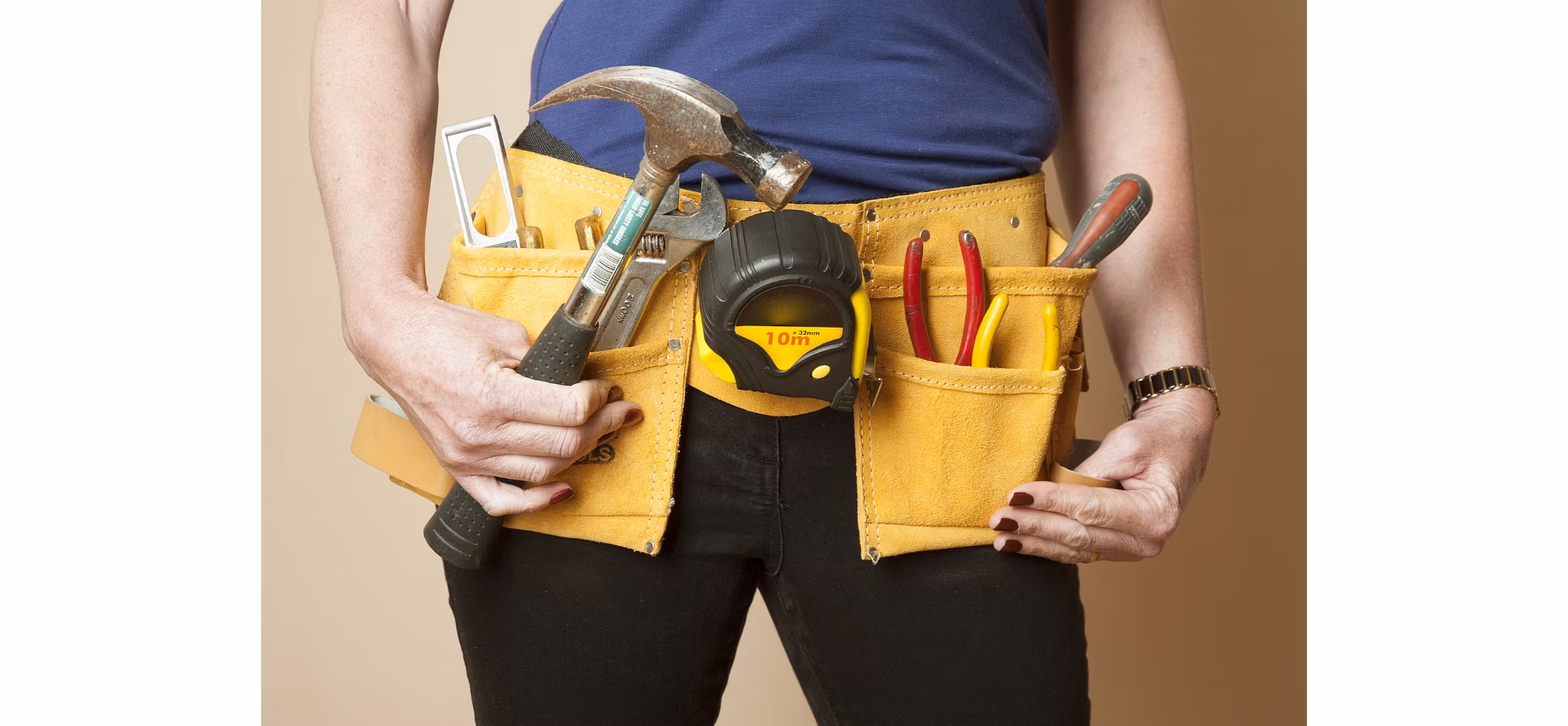 Close-up of a person wearing a tool belt filled with various tools including a hammer, measuring tape, and pliers.