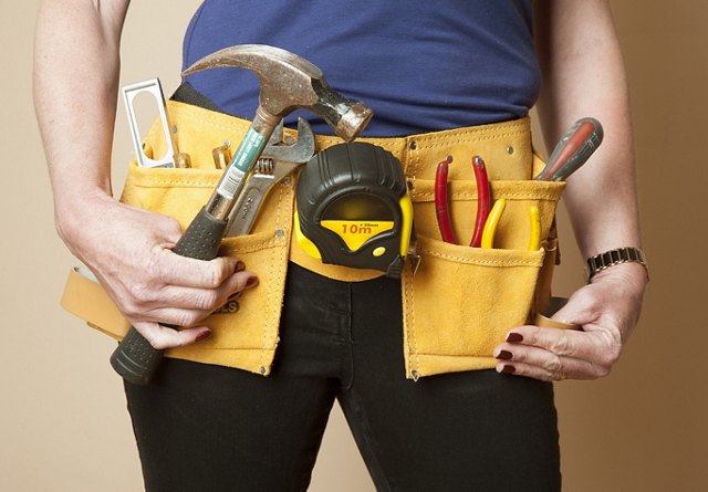 Close-up of a person wearing a tool belt filled with various tools including a hammer, measuring tape, and pliers.