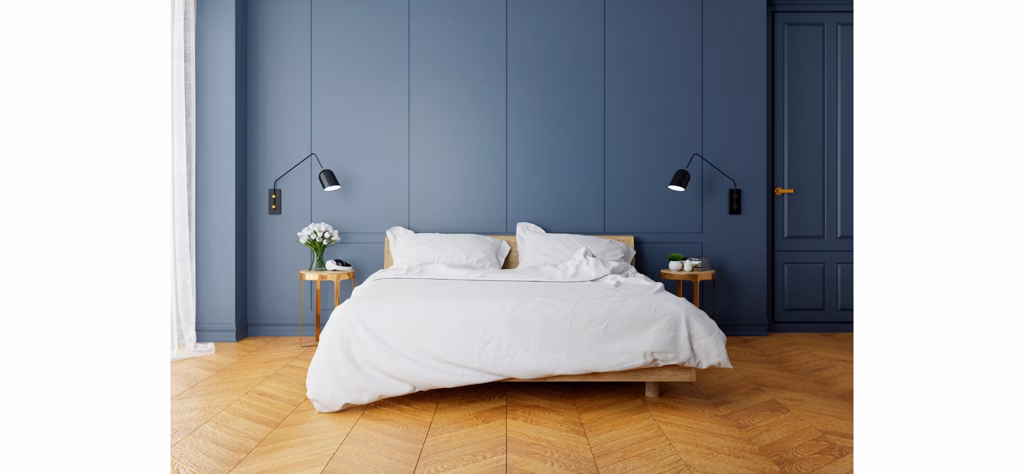 Modern minimalist bedroom with an unmade bed, wooden side tables, and wall-mounted lamps against a dark blue wall.