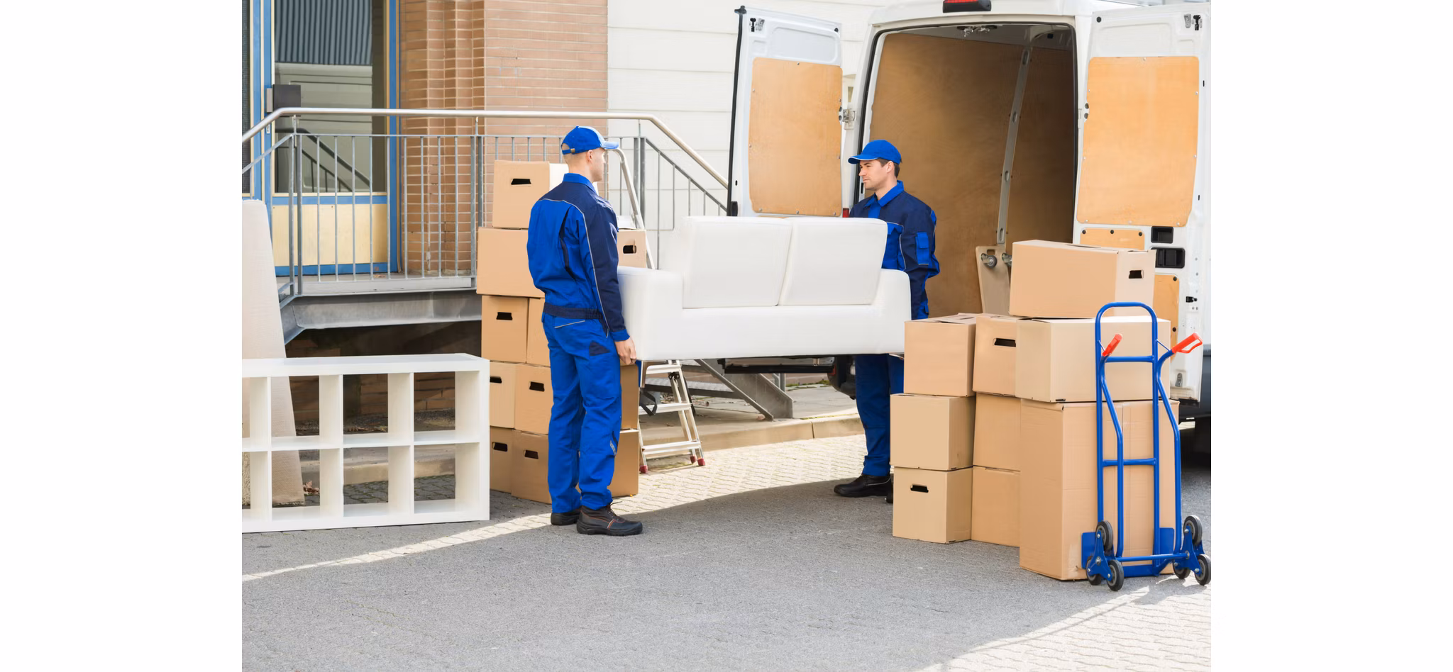 Two movers in blue uniforms loading a white sofa and cardboard boxes into a moving van.
