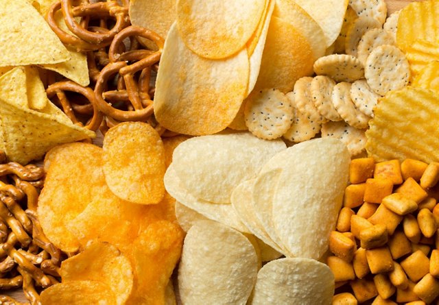 An assortment of snacks including pretzels, chips, and crackers spread out on a wooden surface.