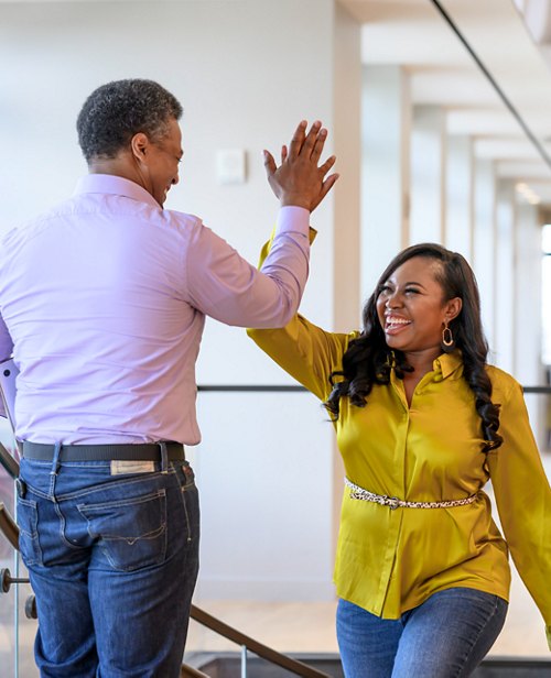 Two cheerful colleagues giving each other a high-five in an office environment, celebrating a success or agreement.