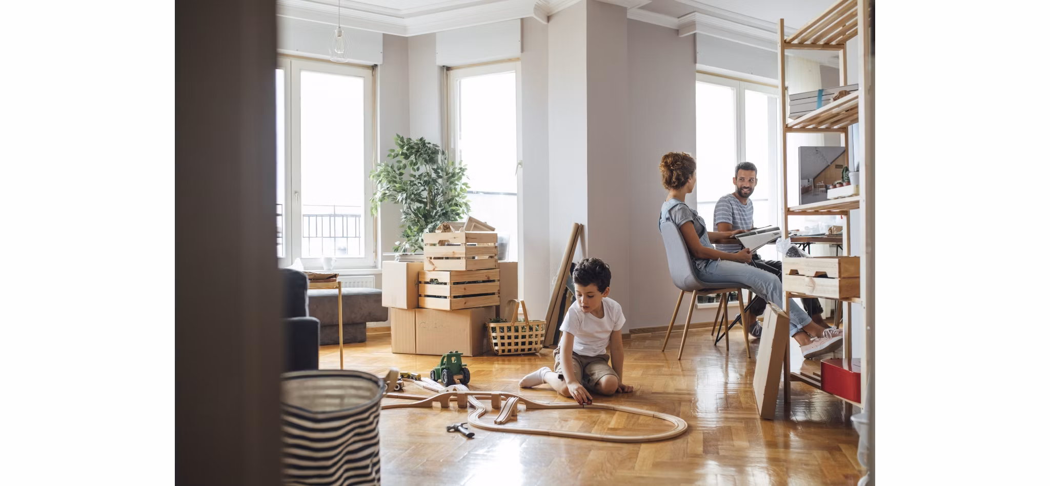 A family settling into a new home, with a child playing on the floor and parents organizing in the background.
