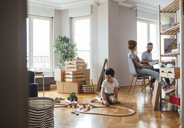 A family settling into a new home, with a child playing on the floor and parents organizing in the background.