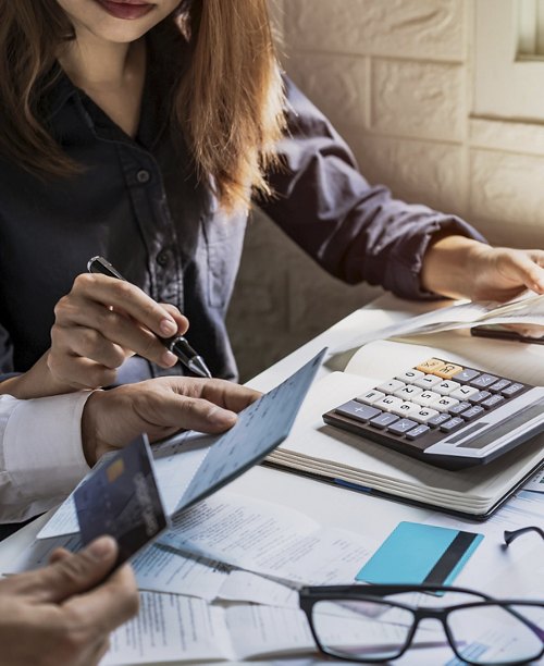 Close-up of a financial review meeting with individuals examining documents and a credit card, with a calculator and eyeglasses on the table indicating a focus on budgeting and expenses.