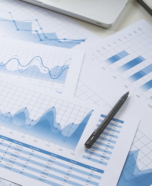 An assortment of printed statistical graphs and charts on a desk, with a pen and a laptop, suggesting analysis for business risk management or performance evaluation.