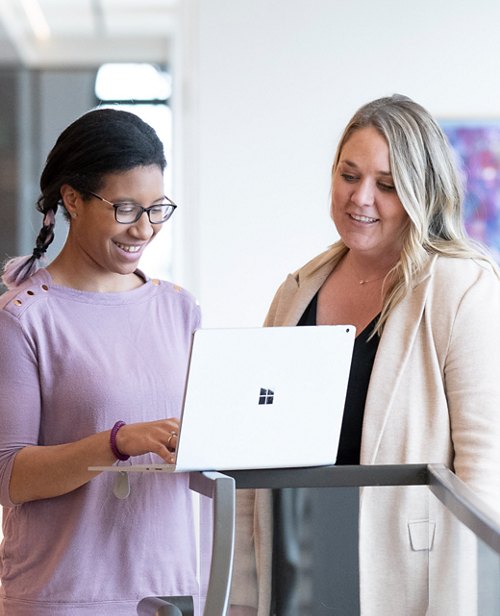 Two professional women collaboratively working on a laptop, engaged and smiling.
