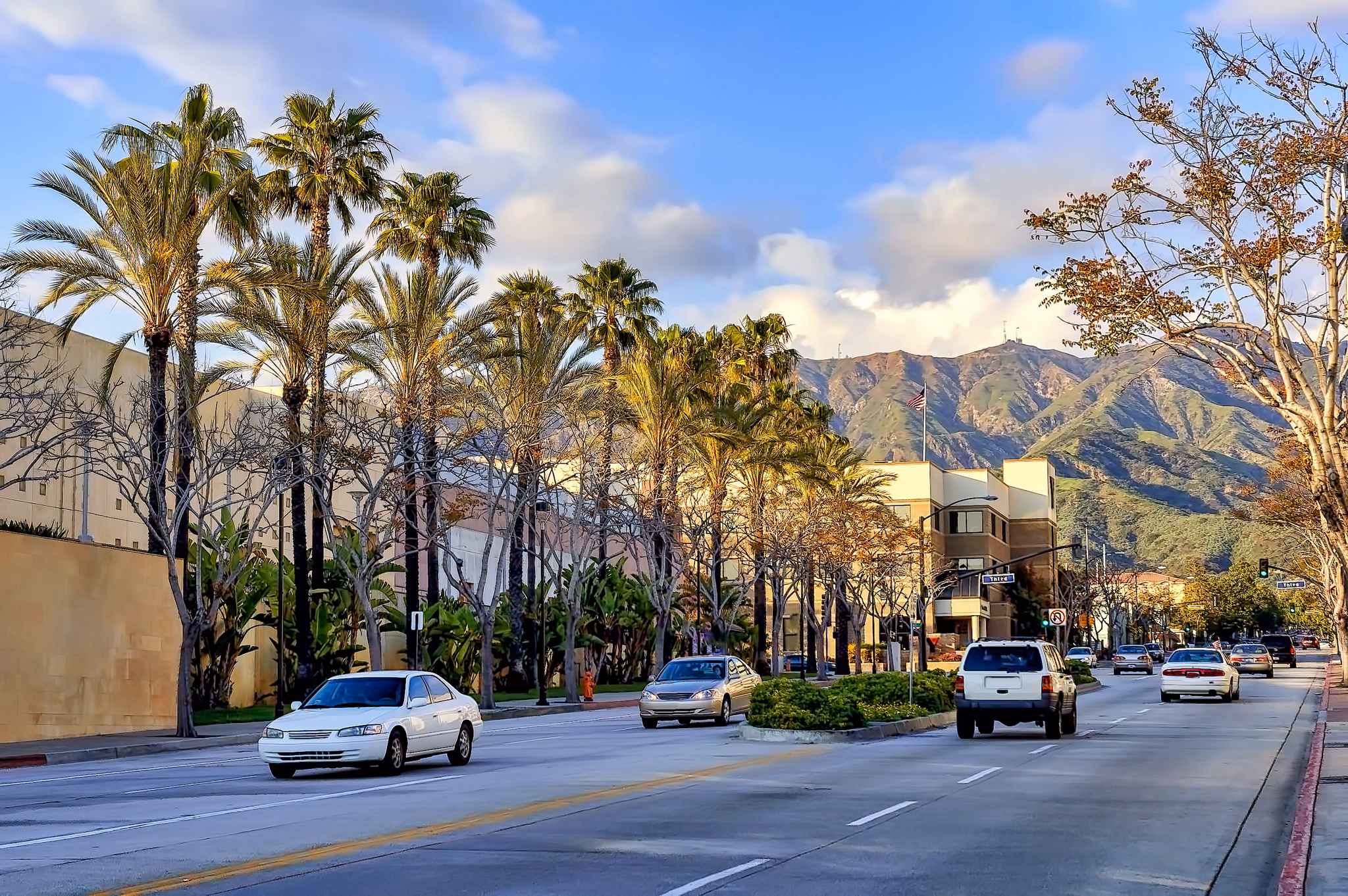 A street in Burbank, California, lined with palm trees and framed by mountains under a blue sky, with cars driving by.