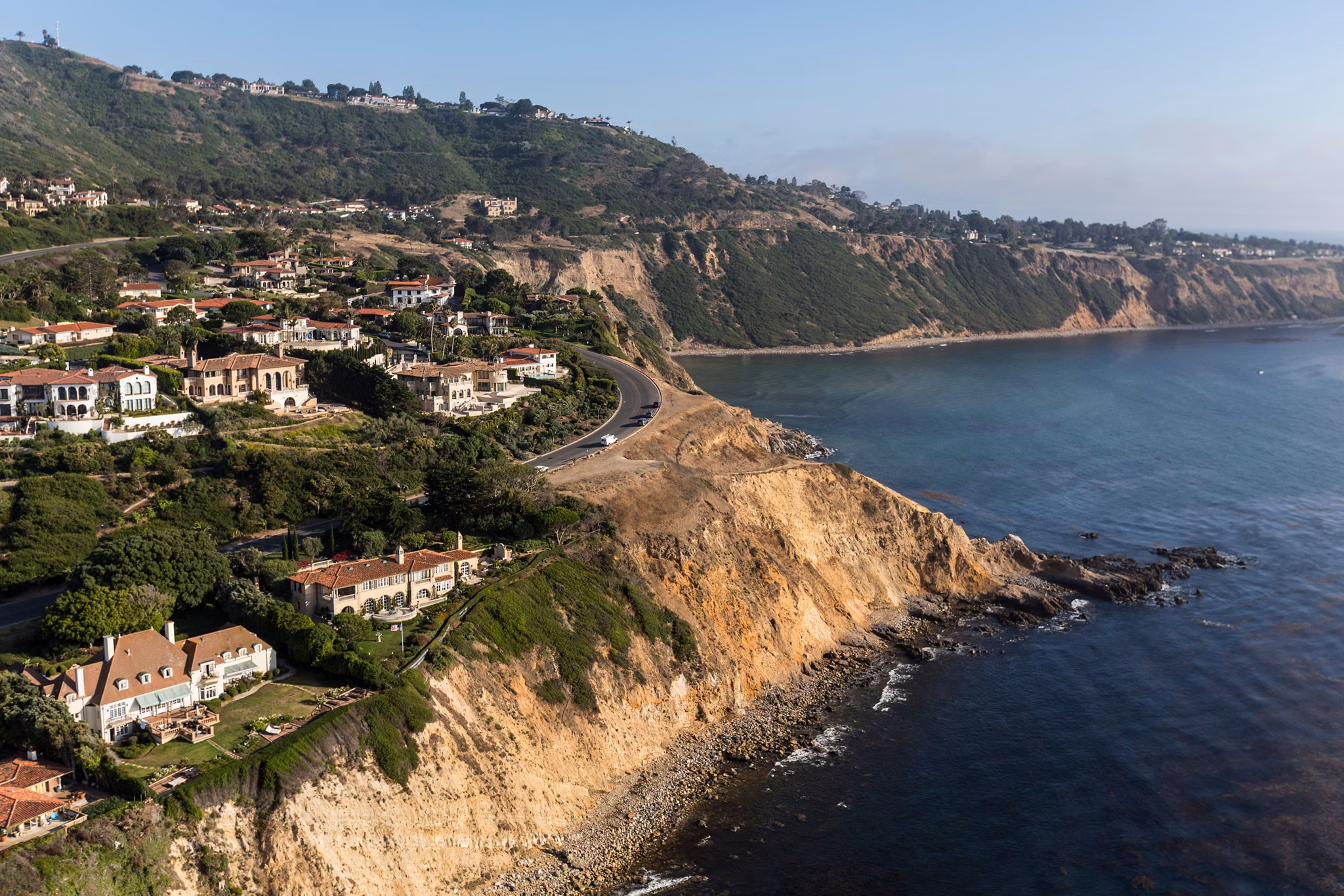 Coastal homes in Culver City, California, overlooking rocky cliffs and the ocean with green hills in the background.