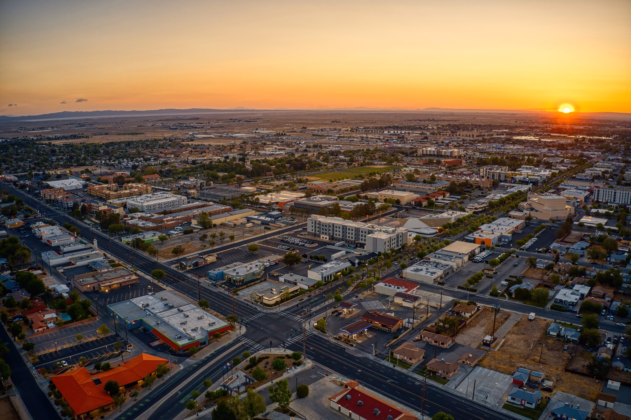 A sunset view over Lancaster, California, showing a mix of buildings, roads, and open land stretching into the horizon.