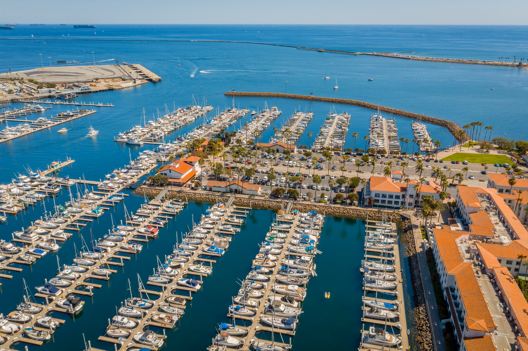 A marina in San Pedro, California, filled with rows of boats and surrounded by buildings with red-tiled roofs along the blue ocean.