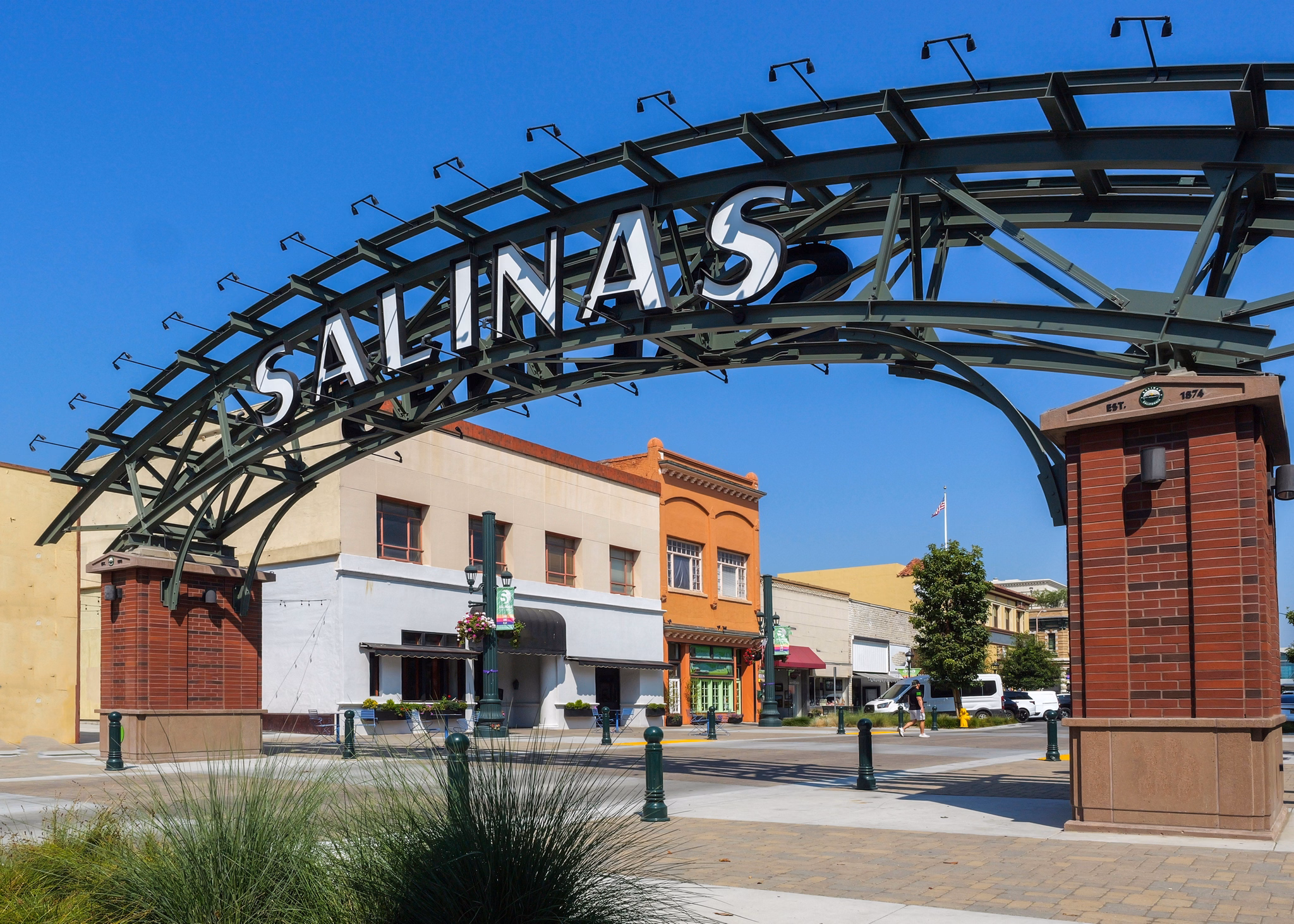 An archway with &quot;Salinas&quot; welcomes visitors to the downtown area in featuring colorful historic buildings under a clear sky.
