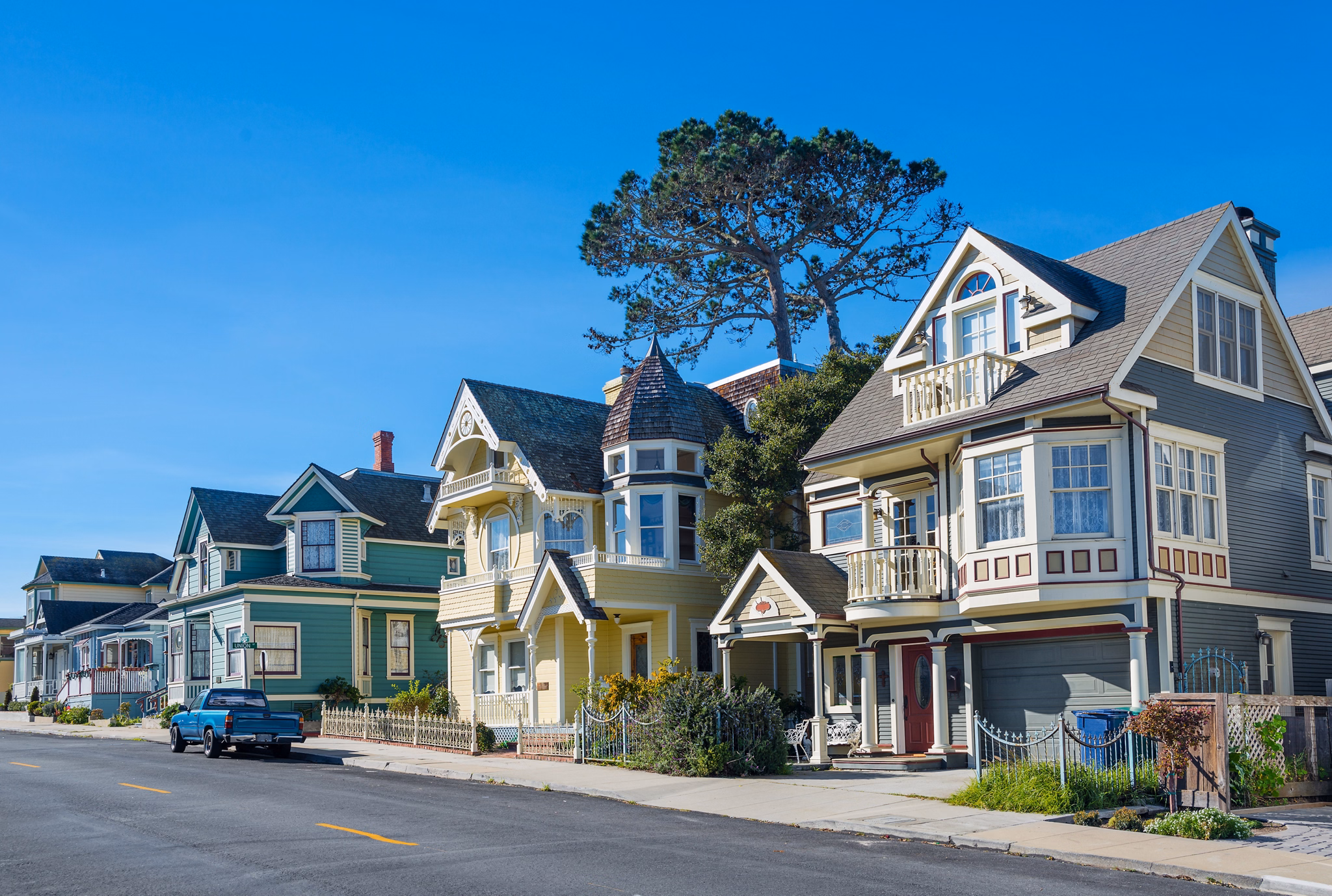 Colorful Victorian-style houses line a quiet street in Monterey, California, under a bright blue sky.