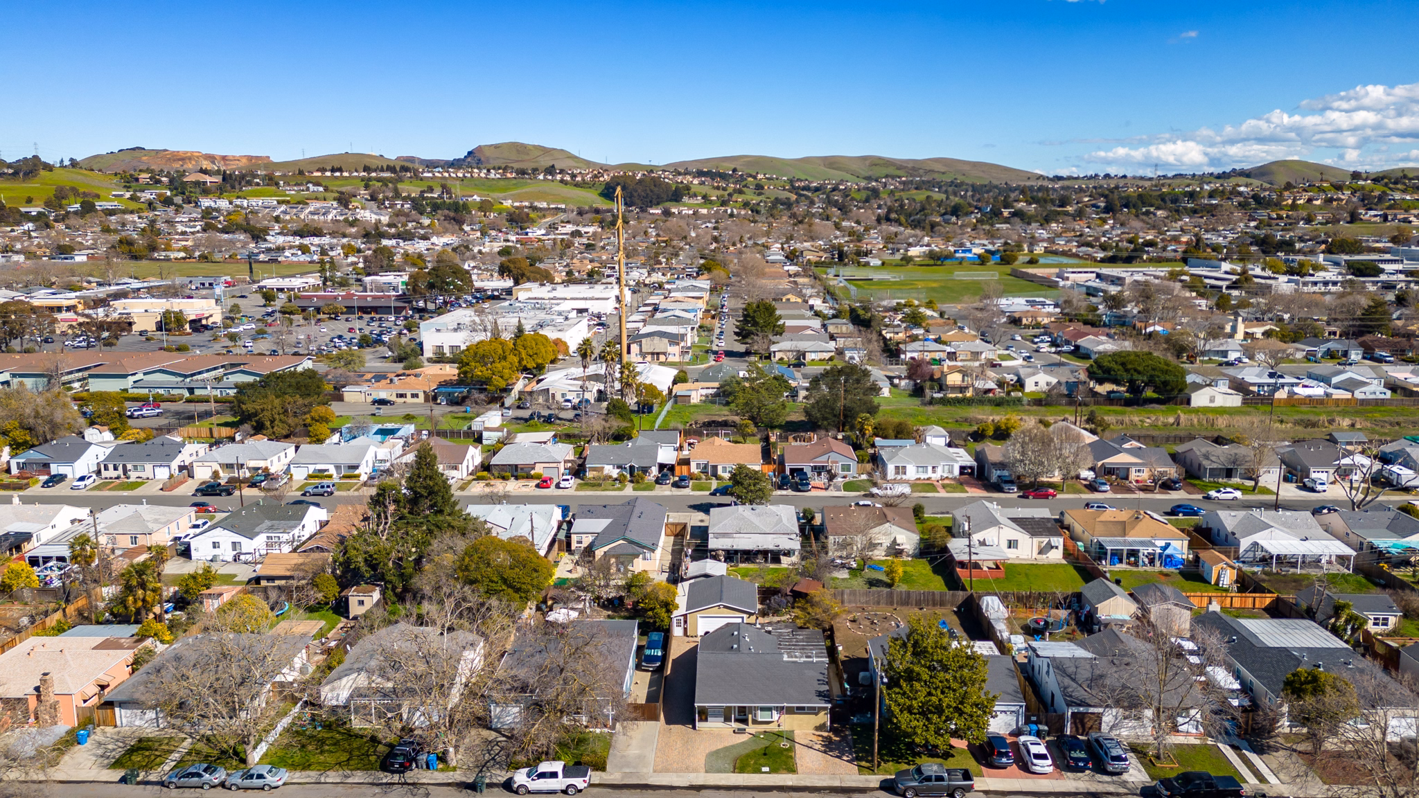 Aerial view of Vallejo, California, showcasing a suburban area with rows of houses, green hills in the background, and a clear blue sky.