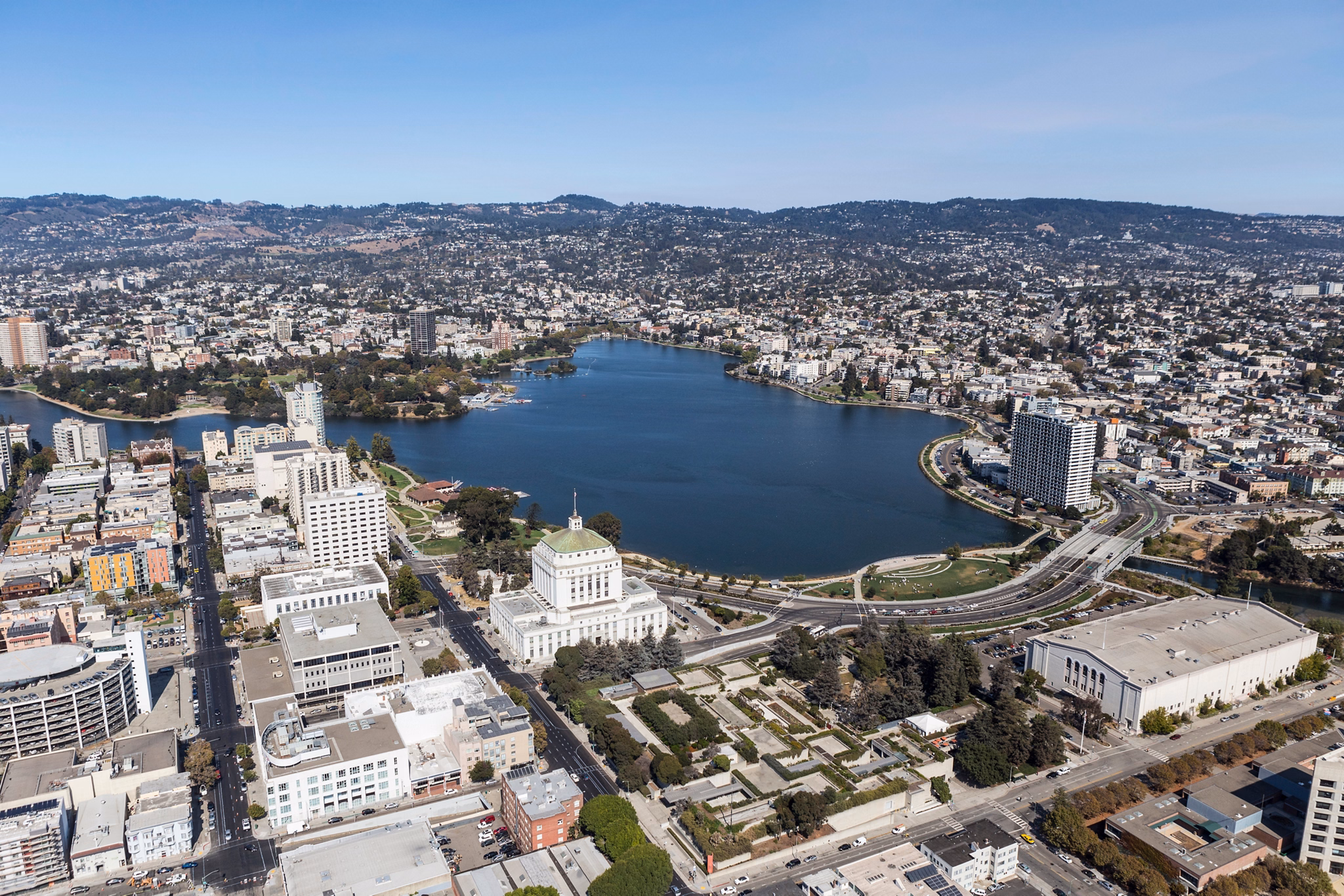 Aerial view of Lake Merritt in Oakland&apos;s East Bay, California, showing urban buildings surrounding the lake with hills in the background.