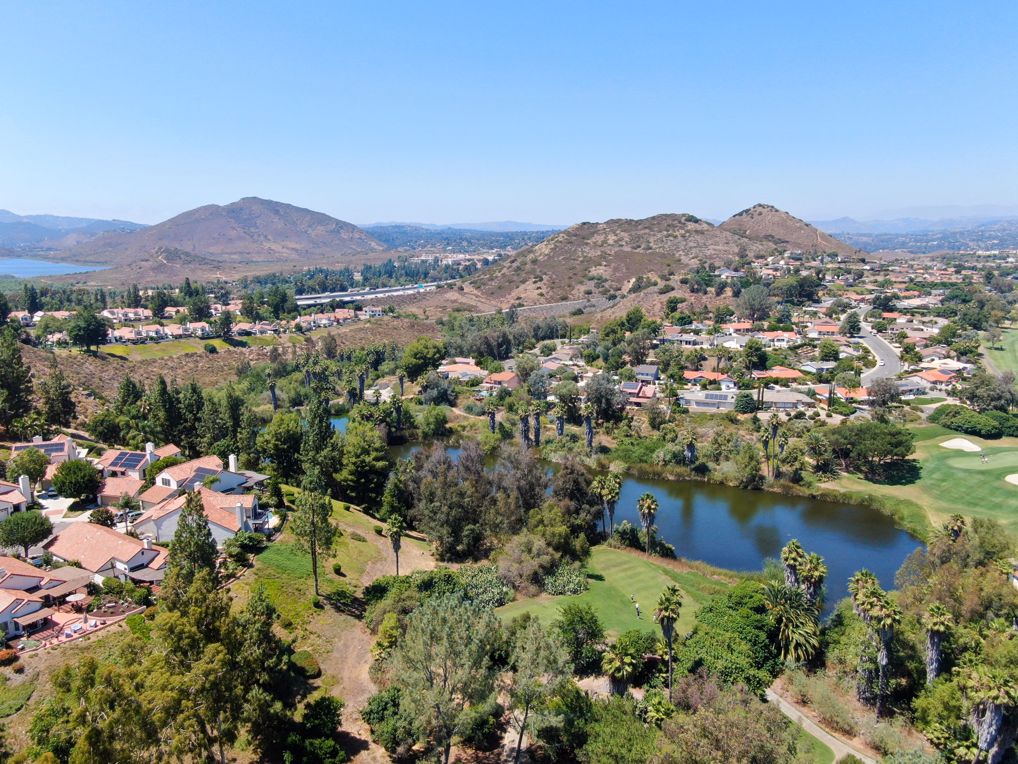 Aerial of La Presa, California showcasing a suburban neighborhood by a lake and mountains.