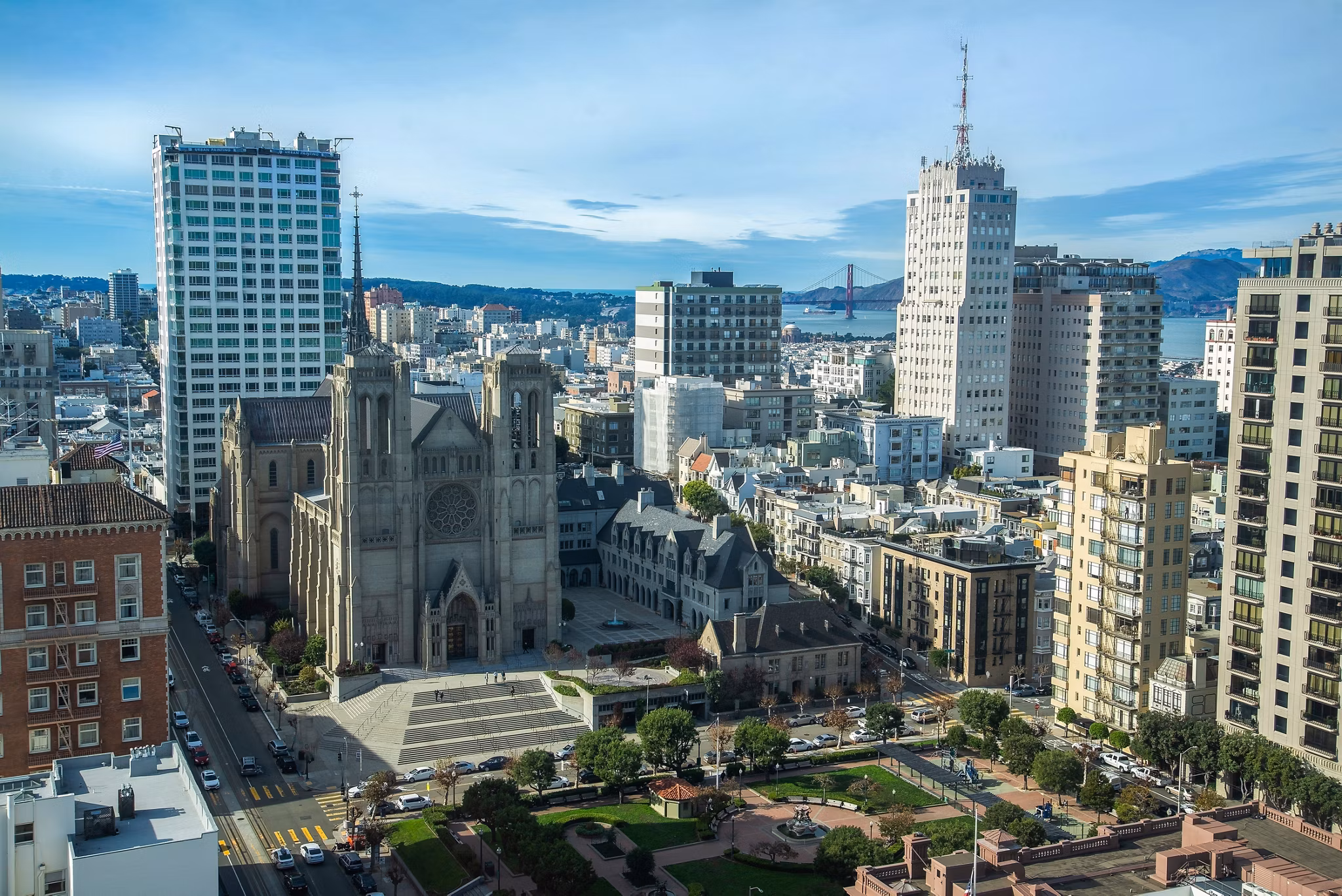 Aerial view of San Francisco, California, highlighting Grace Cathedral, tall city buildings, and the Golden Gate Bridge in the background.