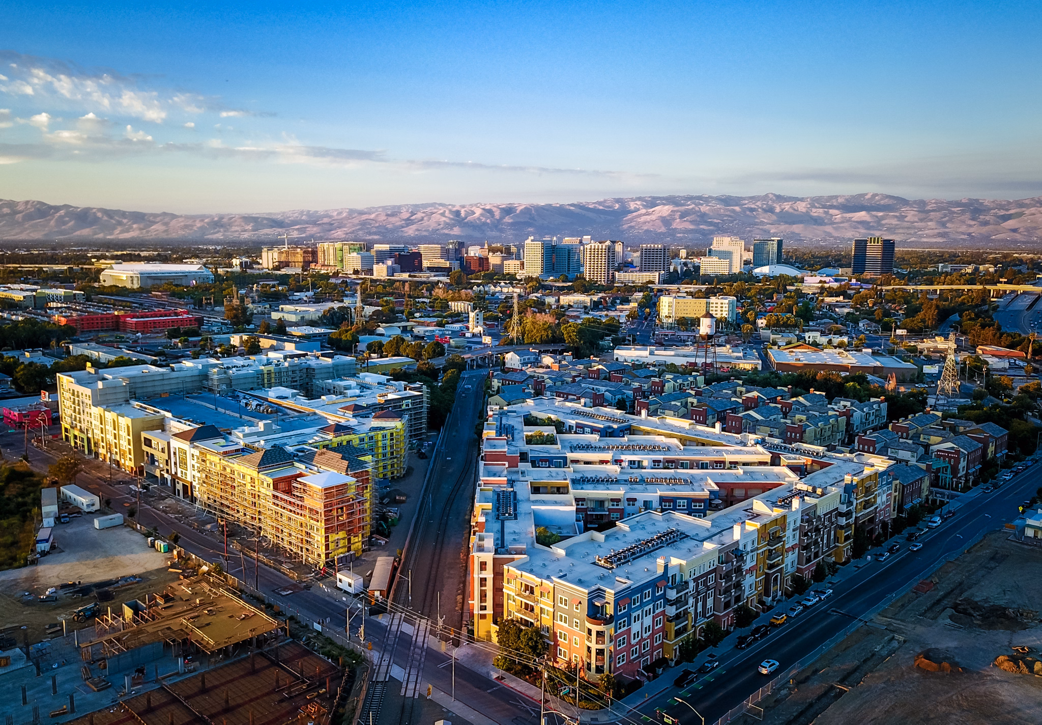 Aerial view of downtown San Jose, California, with colorful apartment buildings in the foreground and mountains glowing pink at sunset.