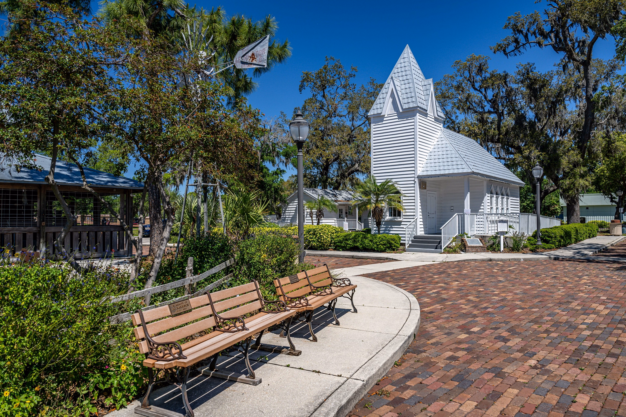 A quaint historic white church with a pointed roof in Palmetto, Florida, surrounded by greenery, brick paths, and wooden benches.