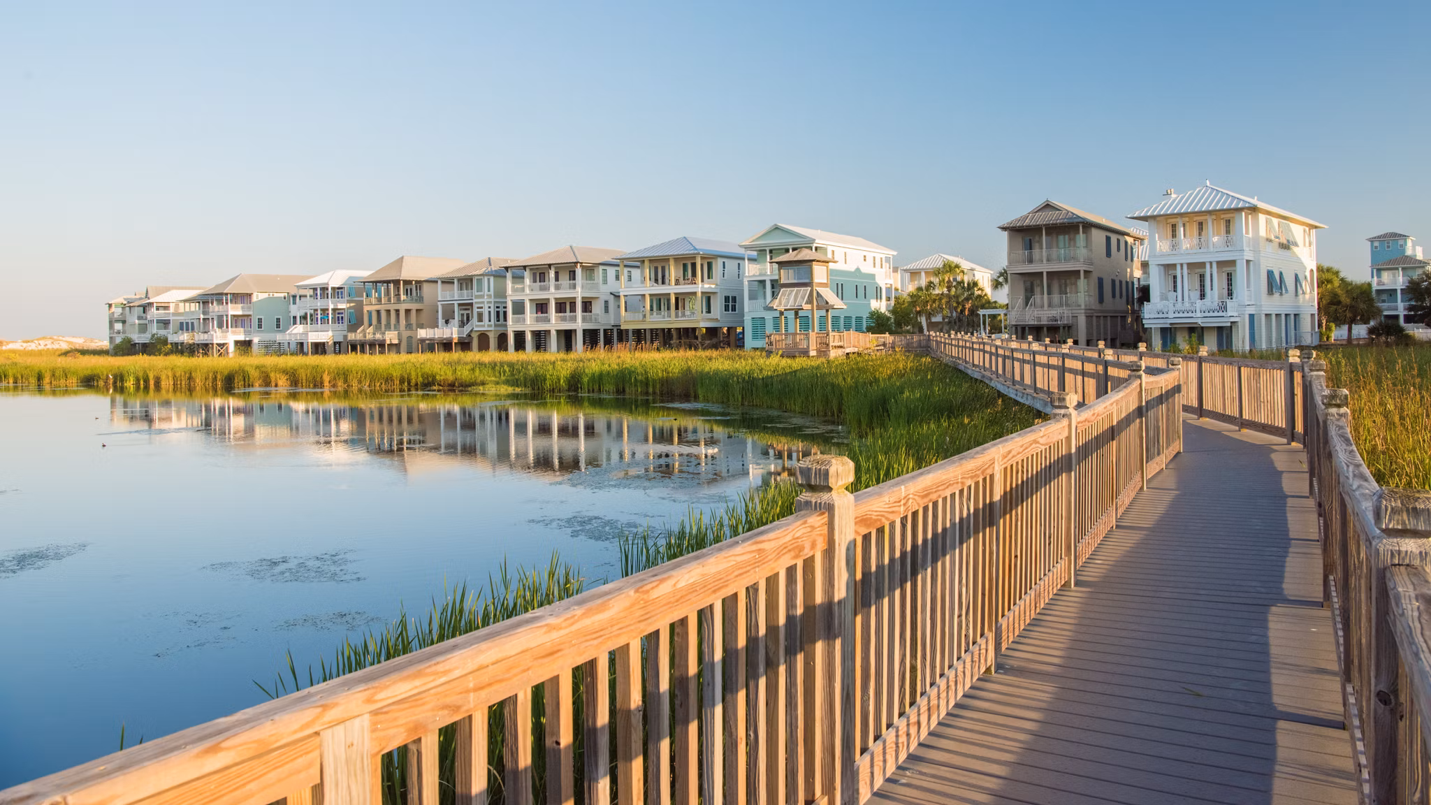 Wooden boardwalk over marshland in the Destin Area, Florida, leading to pastel-colored beach houses built on stilts.