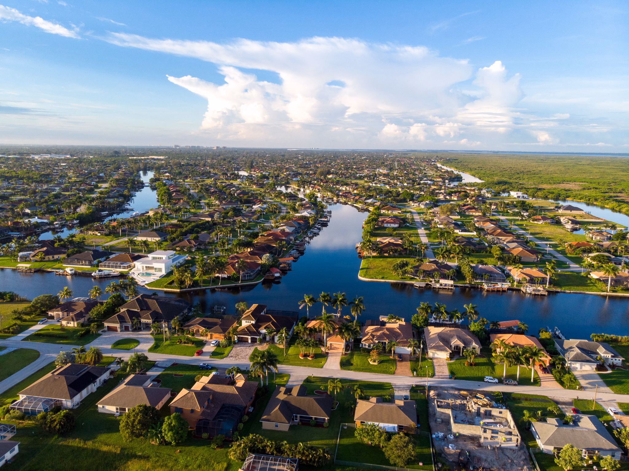 Aerial view of Fort Myers/Cape Coral, Florida, with homes along winding canals, palm trees, and natural wetlands in the distance.