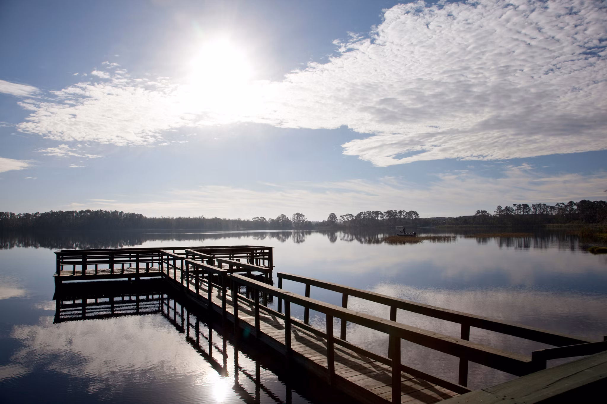 Wooden fishing pier extends over a serene lake in Davenport, Florida, with morning sun reflecting on still waters.