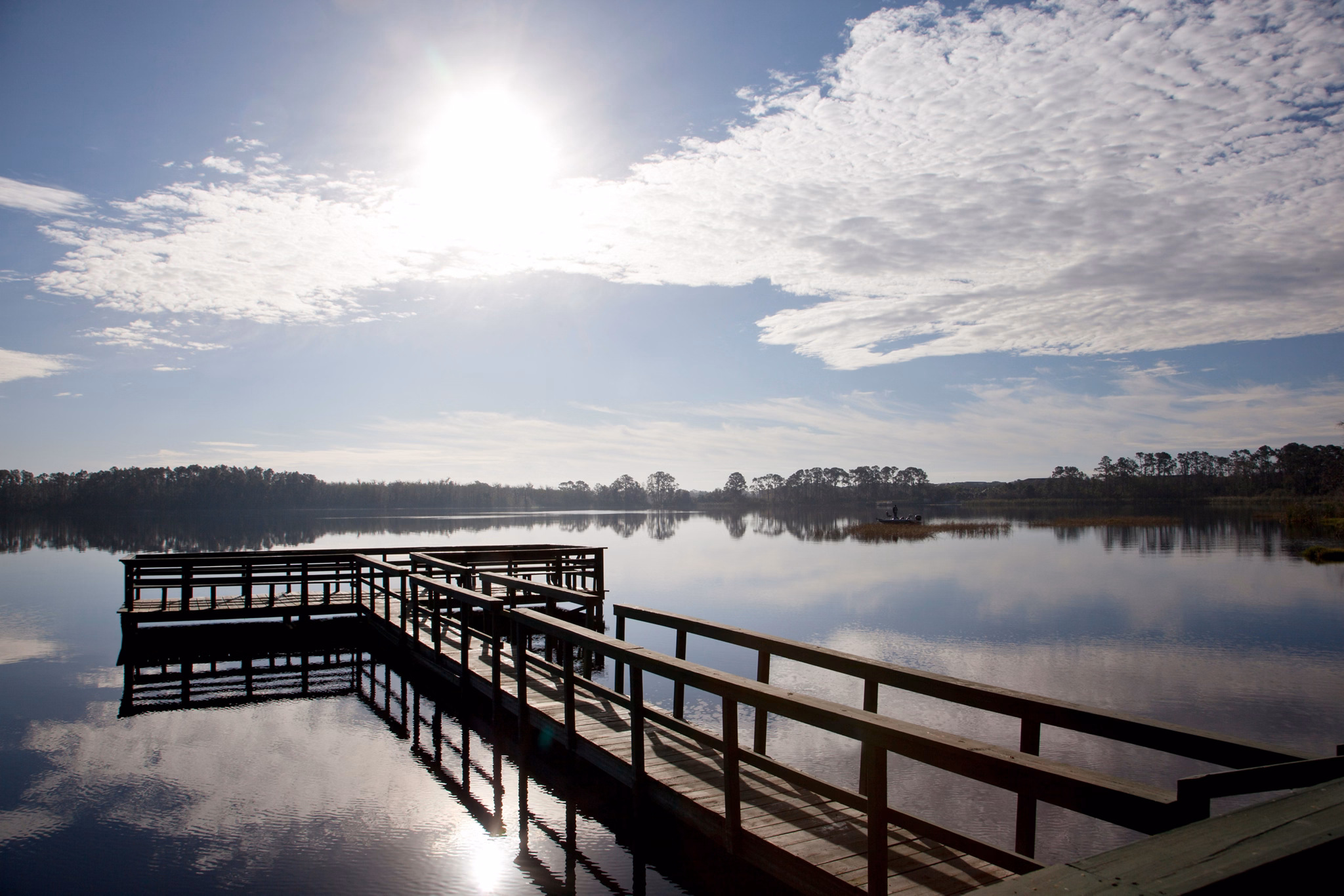 Wooden fishing pier extends over a serene lake in Davenport, Florida, with morning sun reflecting on still waters.