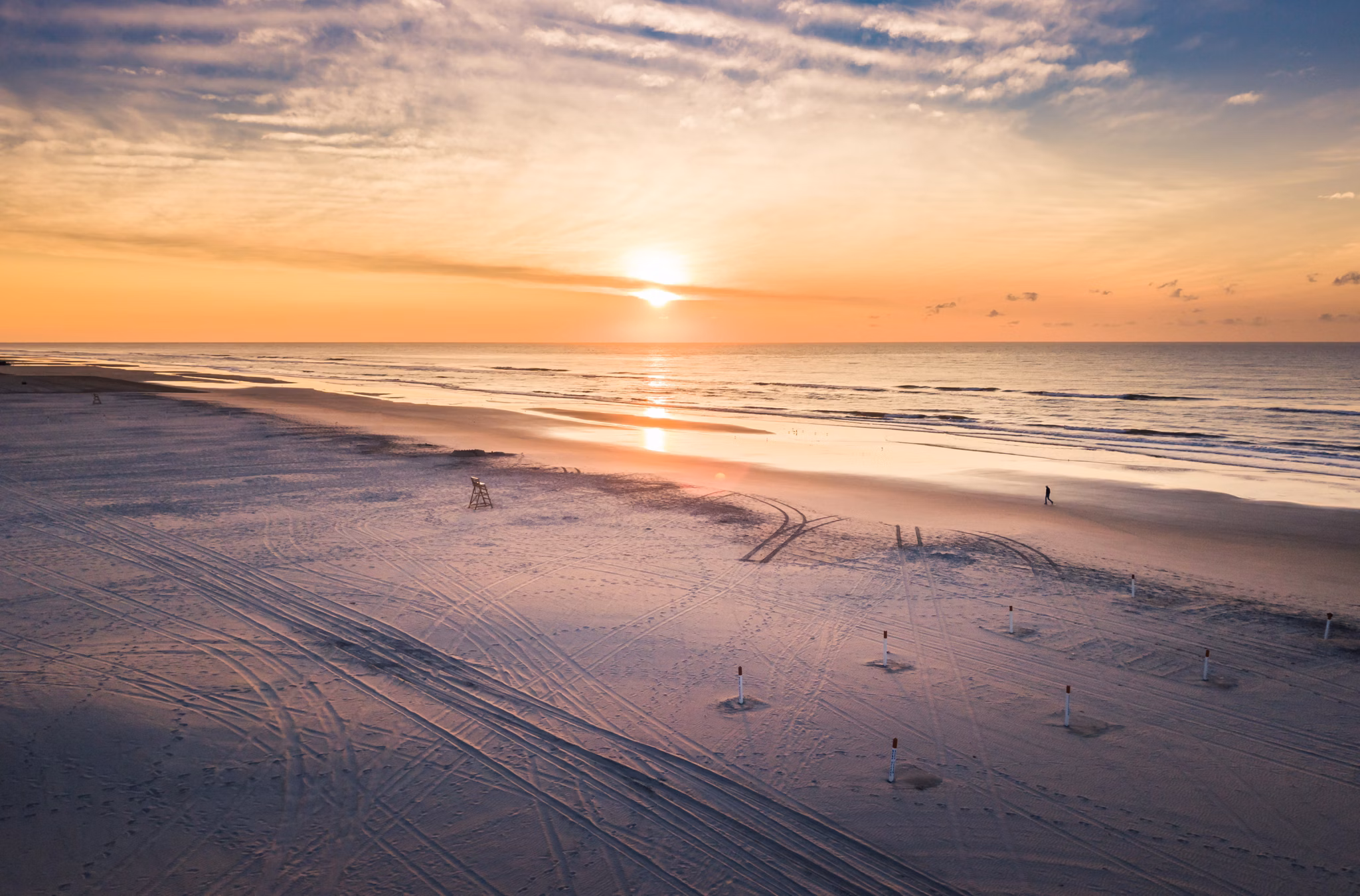 The sunset over a wide sandy beach with tire tracks in Wildwood, Florida