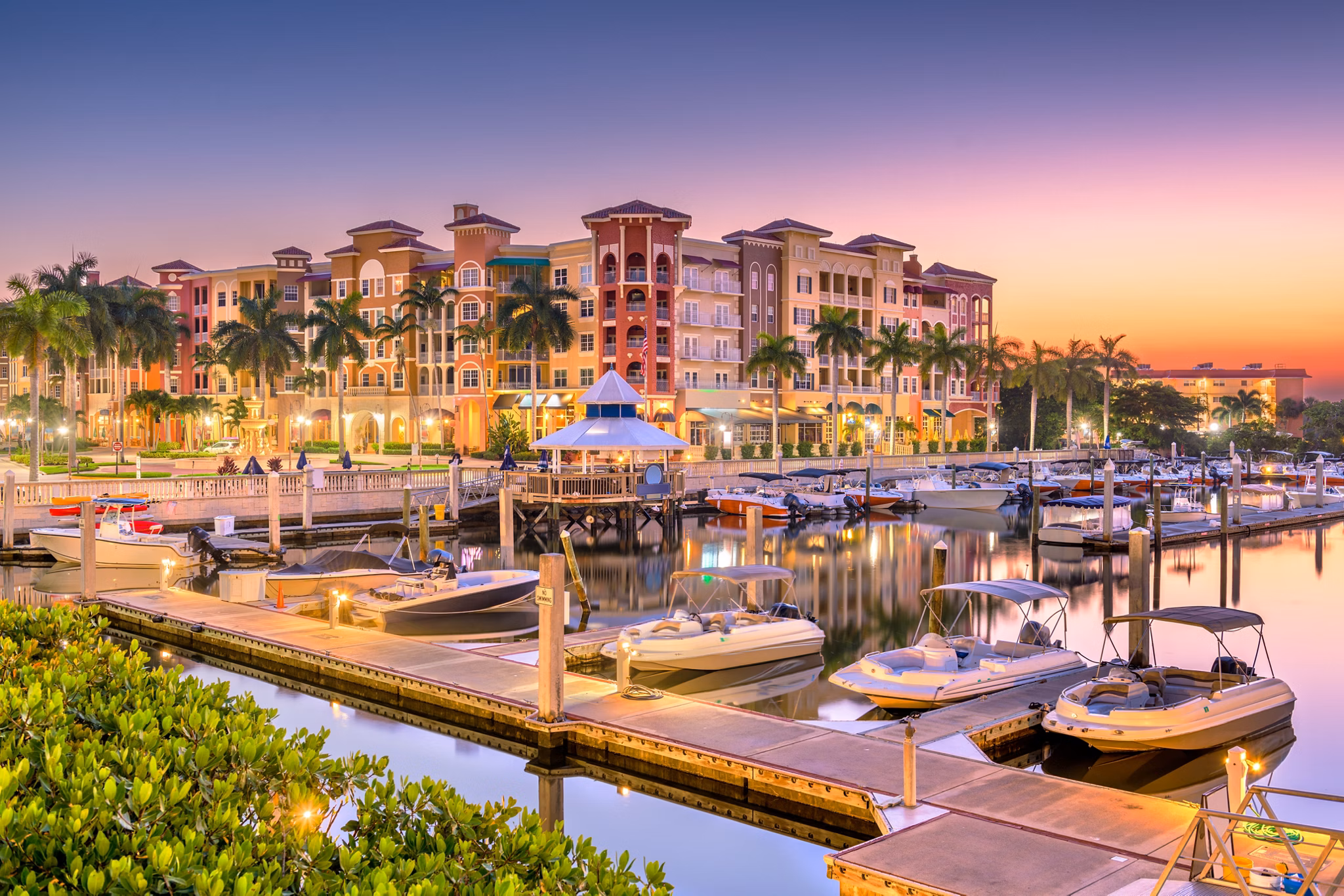 Sunset view of a marina in Naples, Florida with palm tress and multicolored buildings in the background