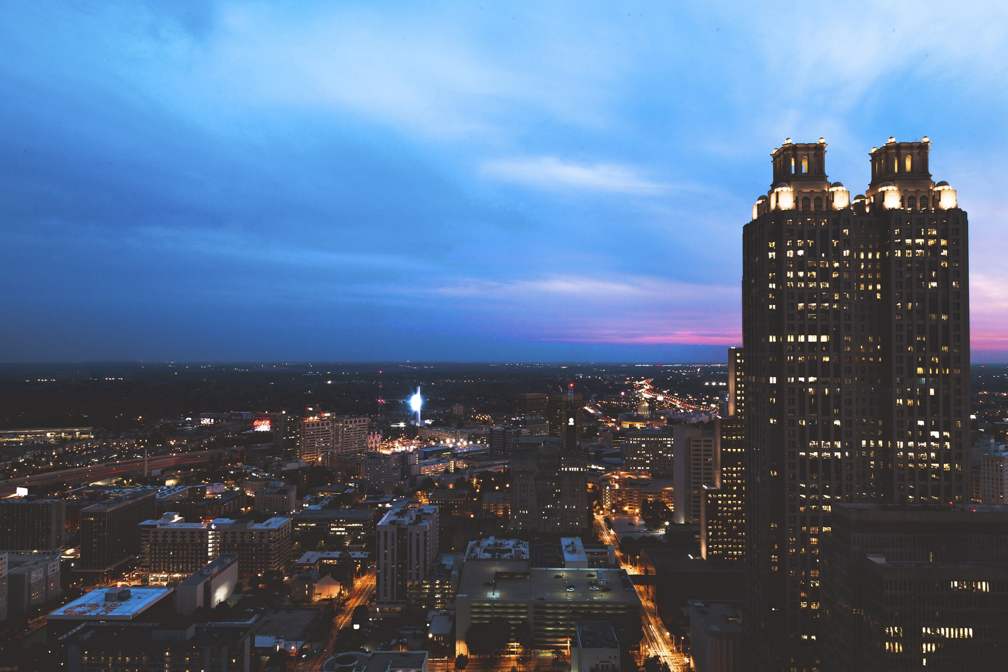 Evening view of Brookhaven, GA with illuminated skyscrapers against dusk sky and city lights stretching to the horizon.