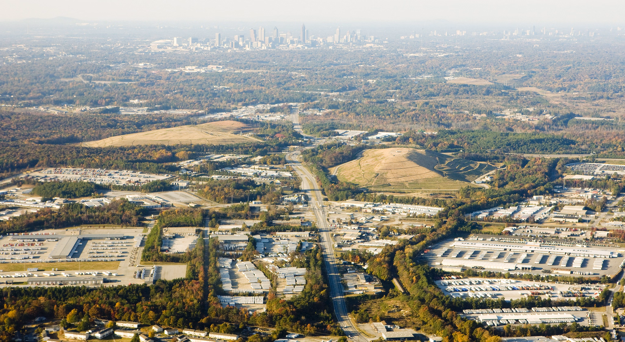 Aerial view of Kennesaw, GA with major highway, industrial parks, autumn trees, and Atlanta skyline visible in distance.
