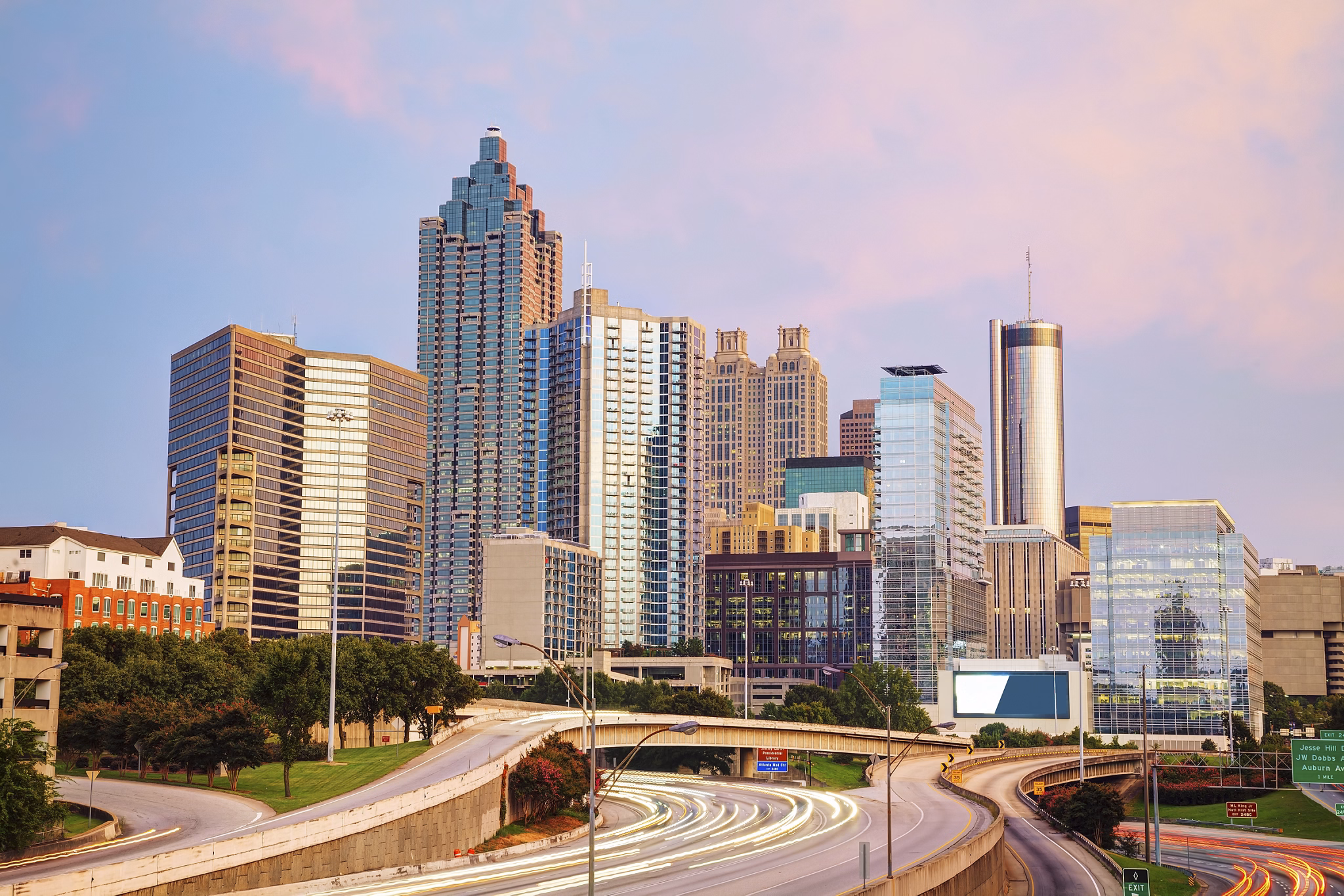 View from Norcross/Peachtree Corners, GA looking toward the Atlanta skyline with glass skyscrapers against a sunset sky.