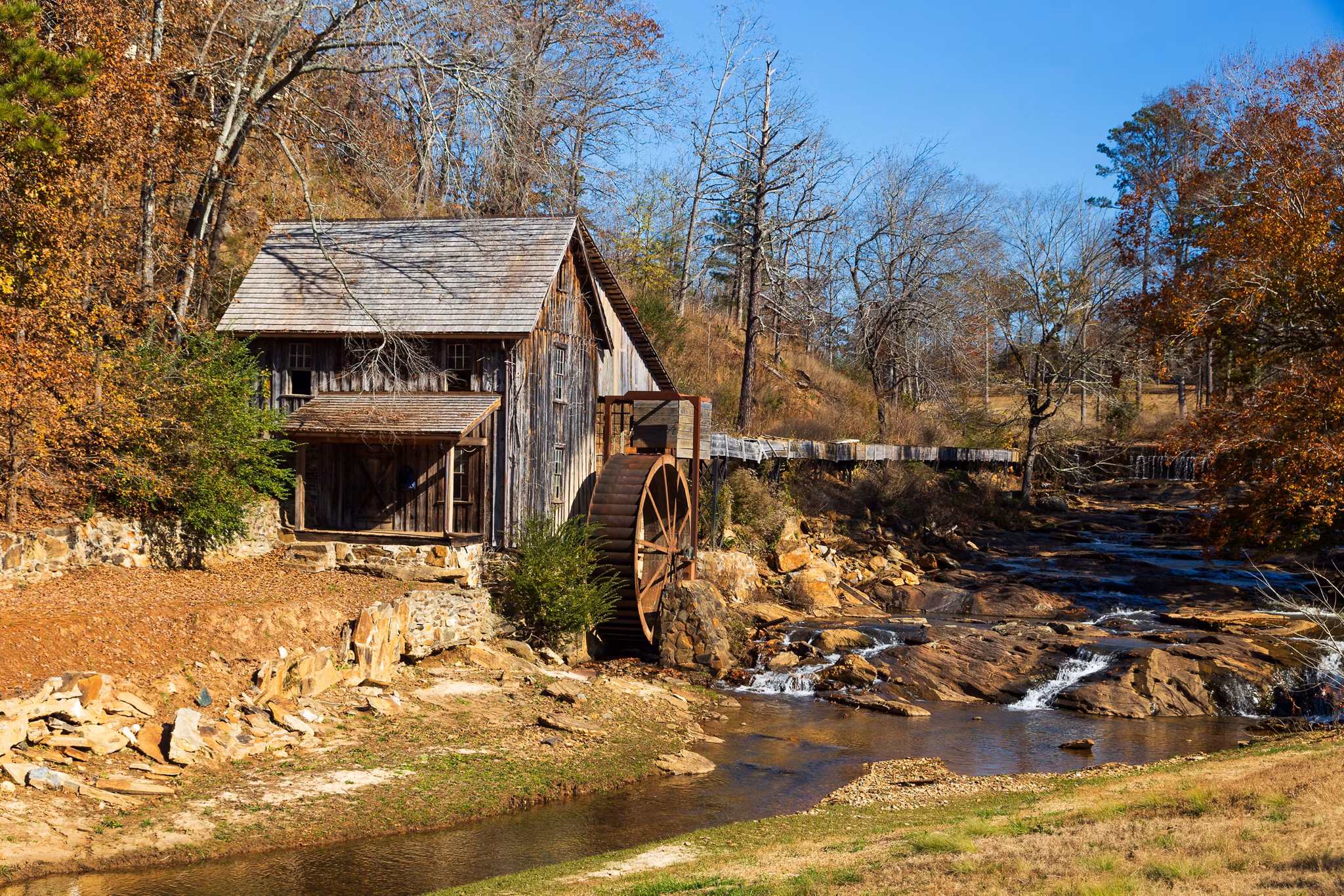Historic wooden grist mill with water wheel in Cherokee County/Bartow County, GA surrounded by autumn trees and a creek.