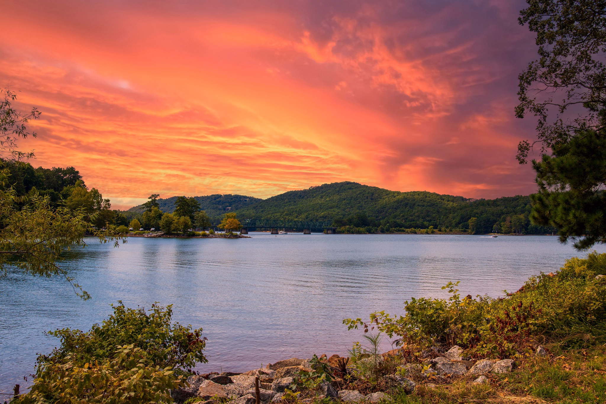 Acworth, GA lake at sunset with orange-pink sky, green mountains in the background, and calm water surrounded by trees.