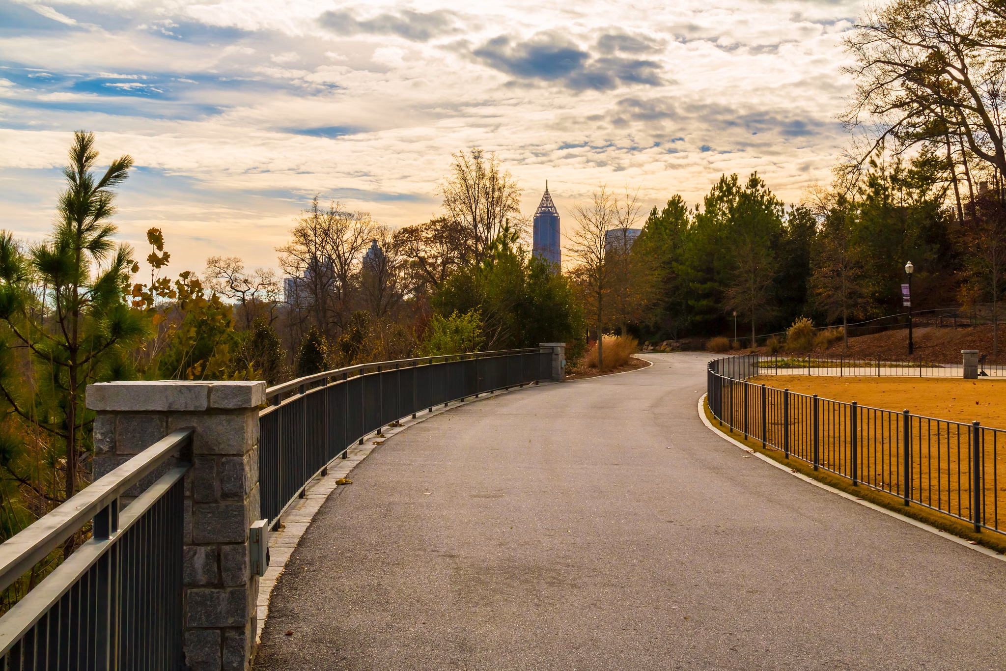 Winding, tree-lined park path in Chamblee, GA with the downtown Atlanta skyline visible in the distance under a cloudy sky.