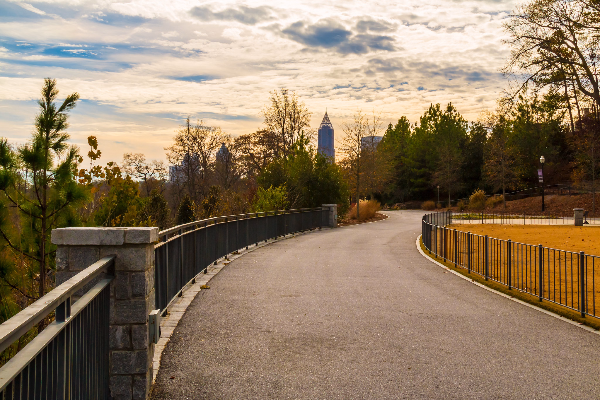 Winding, tree-lined park path in Chamblee, GA with the downtown Atlanta skyline visible in the distance under a cloudy sky.