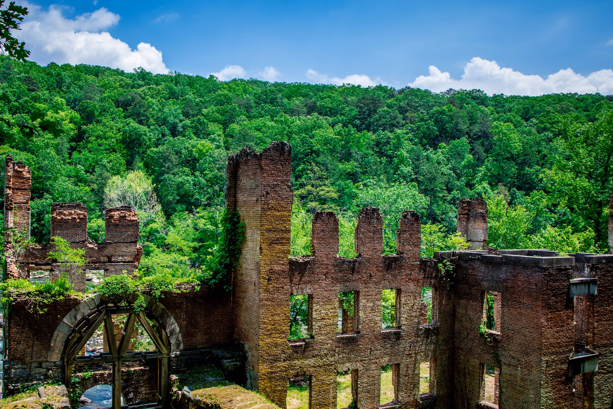 Historic brick ruins of an old mill or factory in Douglas County/Carroll County, GA surrounded by lush green forest.