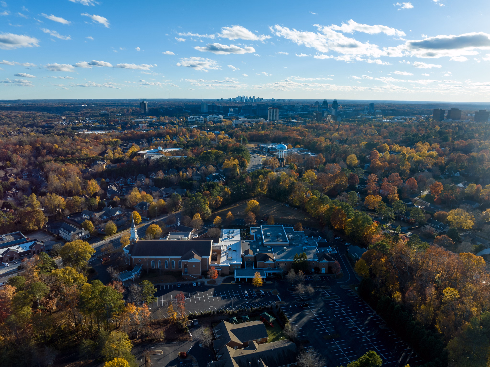 View of Newnan, GA with a large church, autumn trees surrounding neighborhoods, and the Atlanta skyline in the distance.
