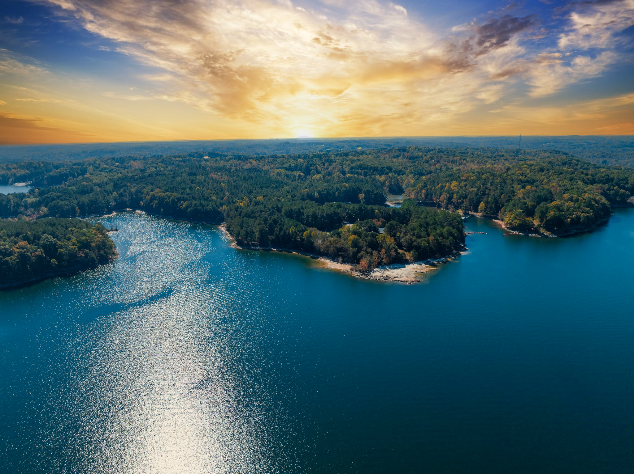 Sunset over Lake Lanier, GA with sparkling blue water, wooded peninsulas, and golden light reflecting across the lake.