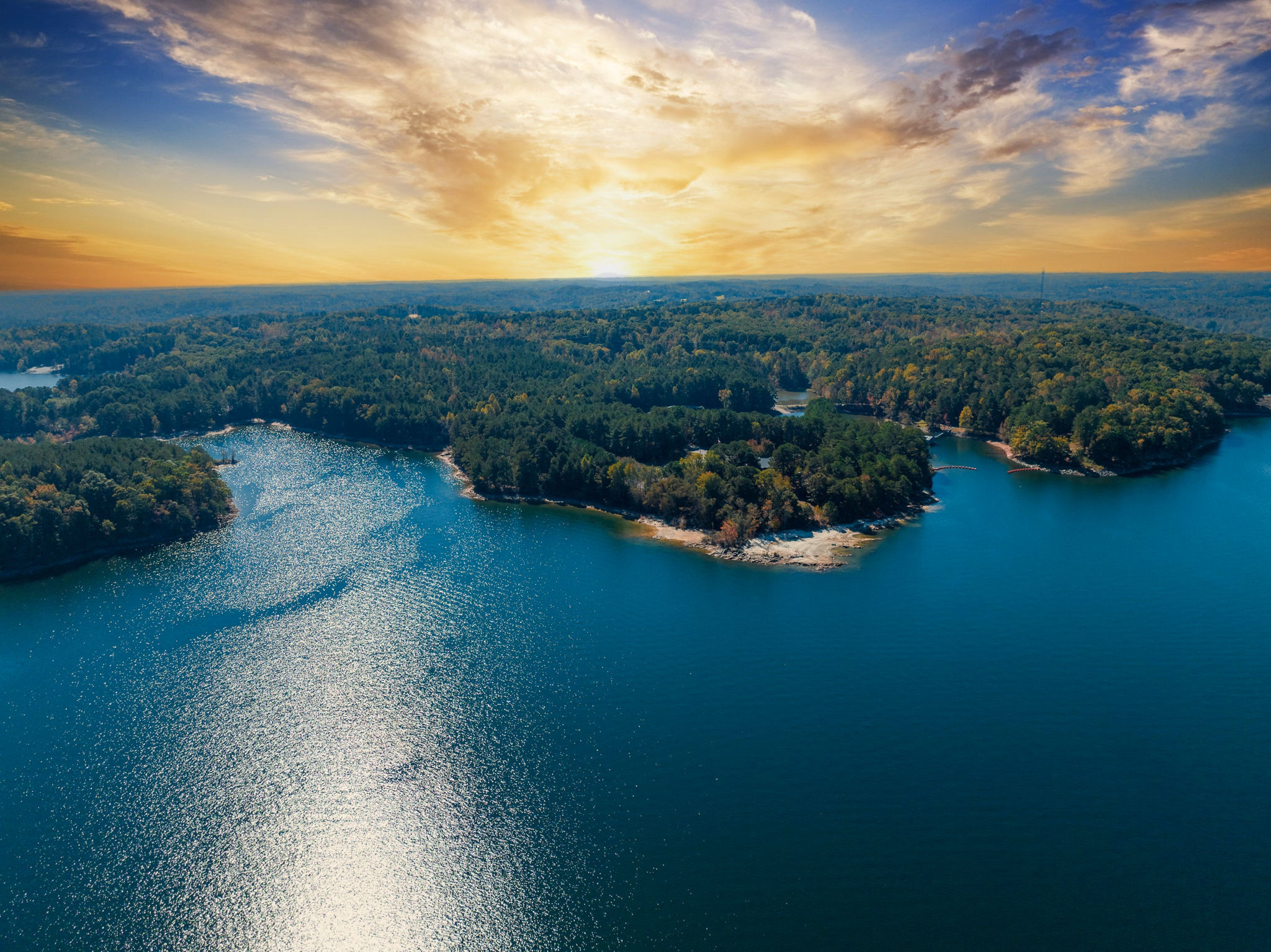 Sunset over Lake Lanier, GA with sparkling blue water, wooded peninsulas, and golden light reflecting across the lake.